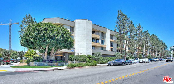 Front view of a multi-story apartment building with balconies and surrounding trees.