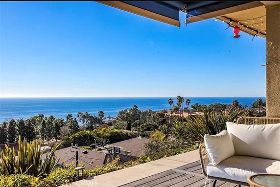 Panoramic view from a patio overlooking the ocean and surrounding lush landscape.