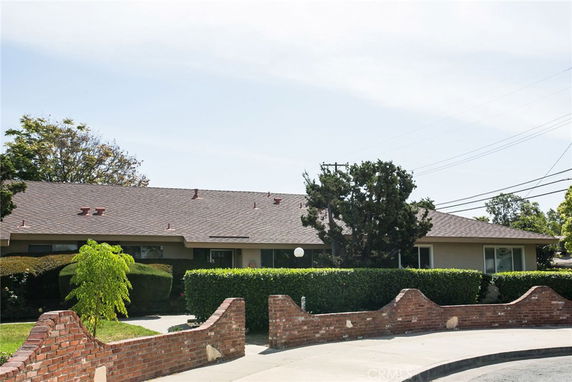Front view of a single-story house with a sloping roof and a brick wall.