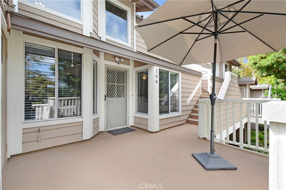 Front view of a house with stairs leading to the entrance and a patio area with an umbrella.