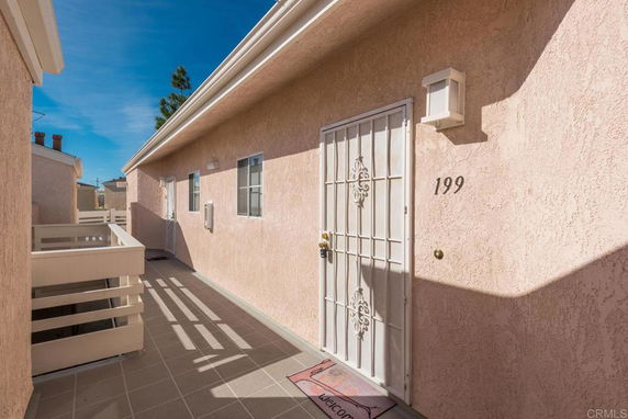 Exterior corridor of a building with a white door marked 199 and a welcome mat.