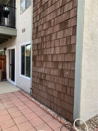 Side view of a house with wood shingle siding and a small patio area.