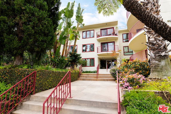 Front view of a multi-story apartment building with balconies and surrounding greenery.