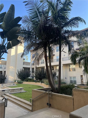 View of a multi-story building with balconies surrounded by palm trees and greenery.
