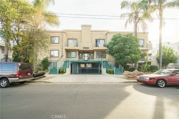 Front view of a two-story apartment building with a gated entrance and stairs leading up to the main doors.