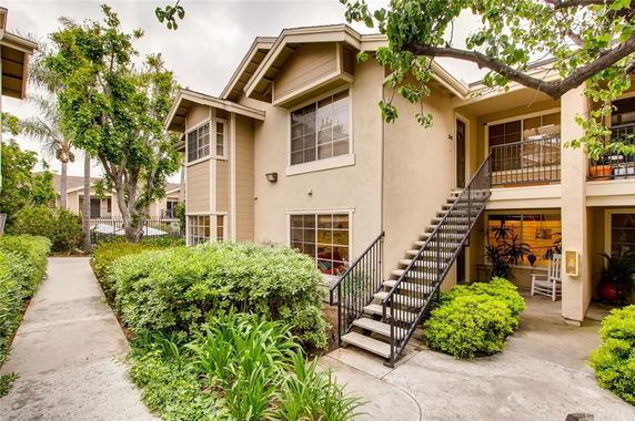 Front view of a two-story residential building with exterior stairs and greenery.