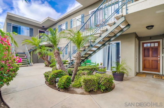Front view of a multi-story residential building with exterior staircases and potted plants.