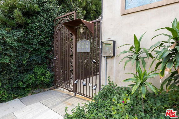 Gated entrance with keypad to a building surrounded by greenery.