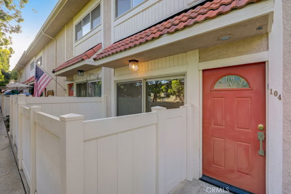 Front view of a townhouse with a red door and a white fence.