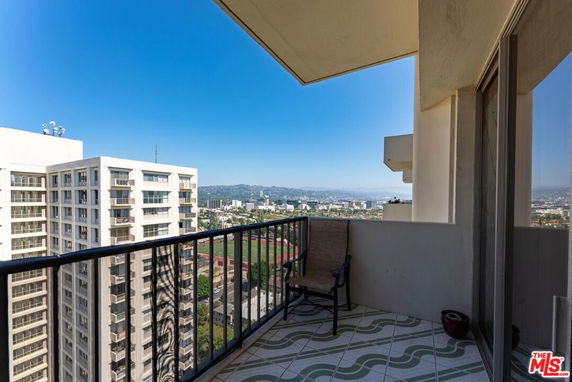 Panoramic view from a balcony overlooking urban buildings and distant hills.