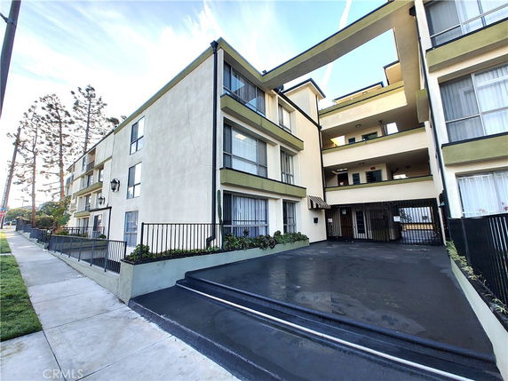 Front view of a multi-story apartment building with balconies and a gated entrance.