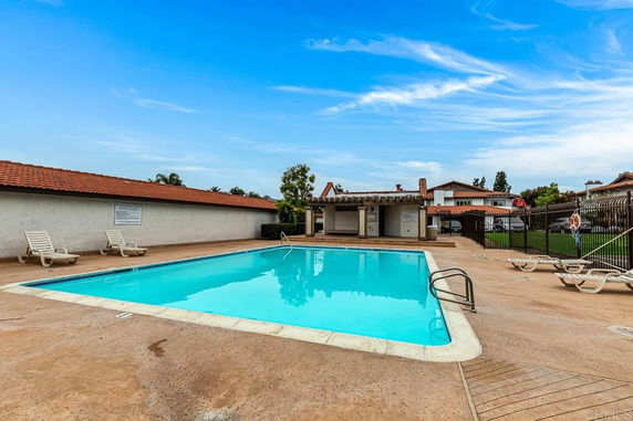 Outdoor swimming pool area with lounge chairs and a small building nearby.