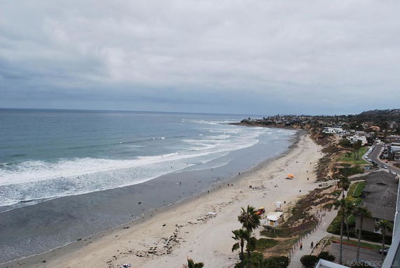 Panoramic view of a beach with ocean waves and adjacent coastal area.