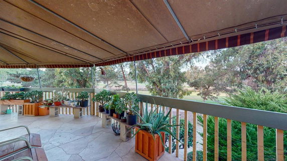 A covered outdoor area with potted plants and railings, overlooking trees and greenery.