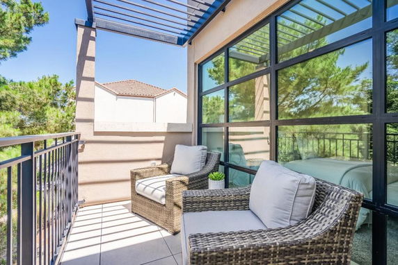 Balcony with wicker chairs overlooking trees and nearby buildings.