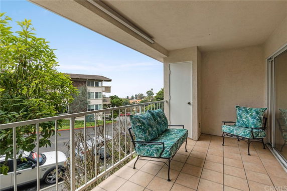 Balcony view with outdoor chairs overlooking a street and nearby buildings.