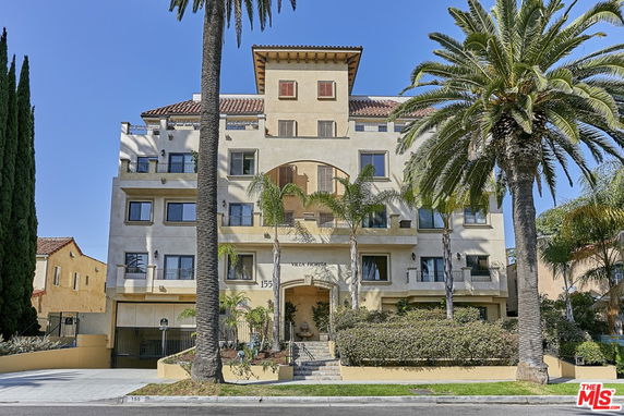 Front view of a multi-story building with balconies and palm trees in front.