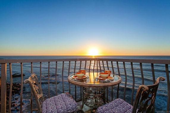 Outdoor balcony with a table and chairs overlooking the ocean at sunset.