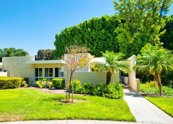 Front view of a single-story house with a flat roof and multiple windows, surrounded by trees and shrubs.