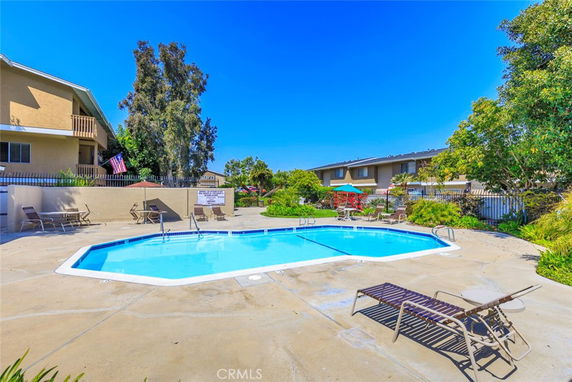 Outdoor swimming pool area with surrounding lounge chairs and a building in the background.