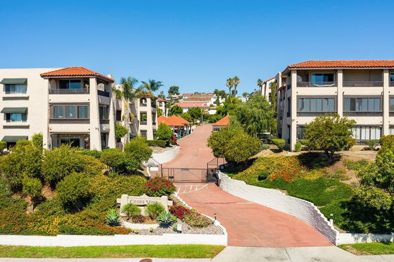 Front view of a multi-story apartment complex with a gated entrance and surrounding greenery.