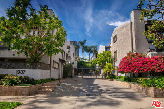 Front view of an apartment complex with a gated entrance and surrounding greenery.