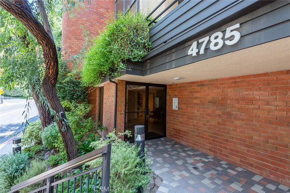 Entrance view of a building with brick exterior and green foliage.