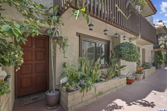 Front view of a house with a wooden door and a balcony with potted plants.