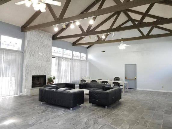 Indoor area with high ceiling featuring exposed beams, a tiled fireplace, sofas, and chairs around a table.