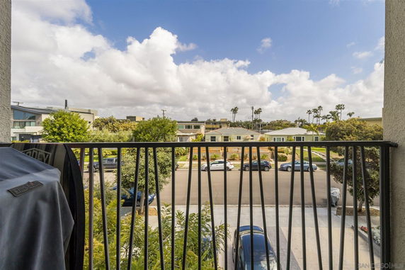 View from a balcony overlooking a residential street with parked cars and houses.