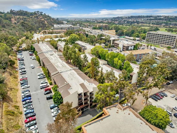 Aerial view of a residential complex surrounded by parking areas and greenery, with a cityscape in the background.