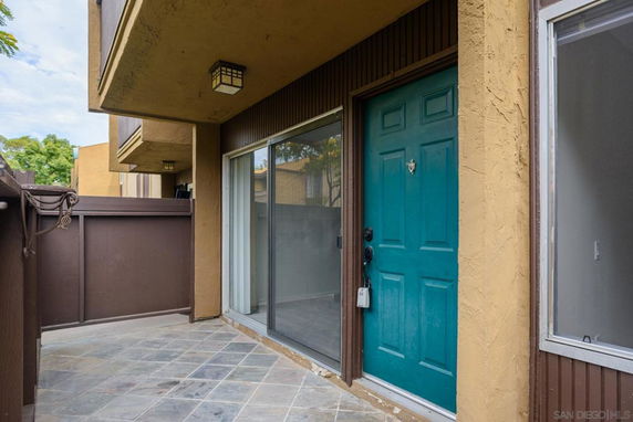 Front entrance of a residential building with a teal door and sliding glass window.