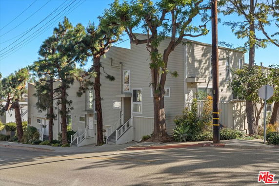 Front view of a multi-story building on a sloped street with trees nearby.