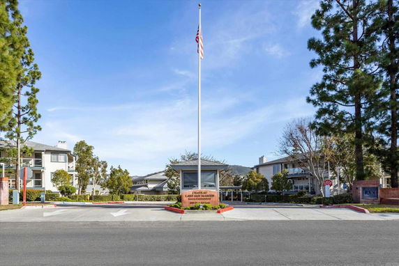 Entrance view of a residential complex with multiple buildings and a central flagpole.