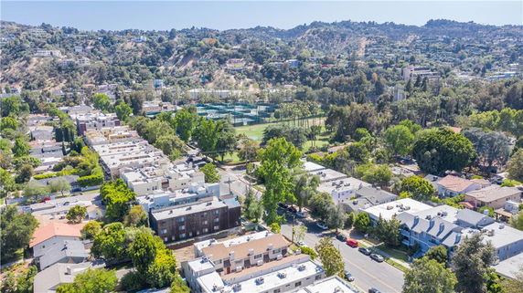 Panoramic view of a residential area with multiple buildings and greenery, surrounded by hills.