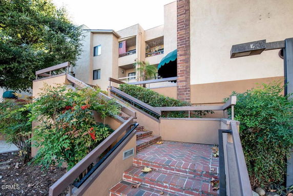 Front view of a multi-story residential building with brick steps and greenery.