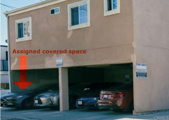 Covered parking area with multiple cars parked underneath a building.
