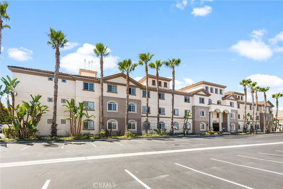 Front view of a multi-story building with palm trees and a parking area.