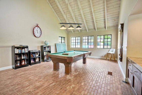 Room with a pool table, bookshelves, and large windows.