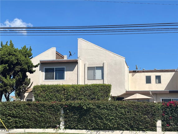 Front view of a beige multi-story house with unique angled rooflines and satellite dishes.