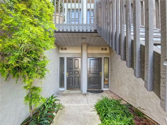 Front view of a building entry with two black doors and surrounding greenery.