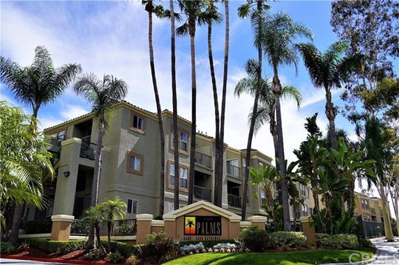 Front view of a multi-story building with balconies and palm trees in the foreground.