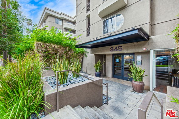 Front view of a multi-story building with entrance and plants.