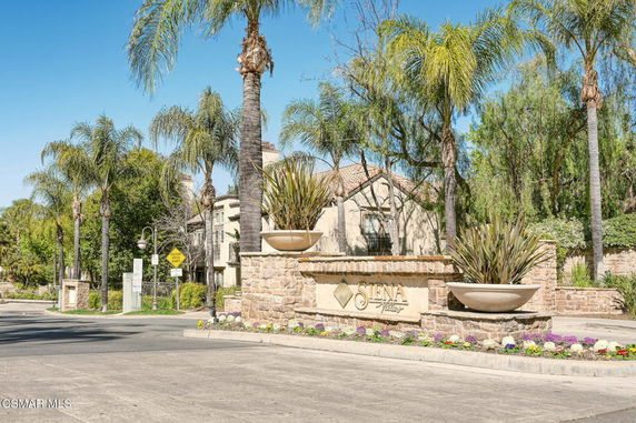 Front view of an entrance to a residential community with stone walls and palm trees.