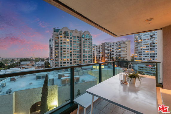 Panoramic view from a building balcony overlooking a cityscape with high-rise buildings at sunset.