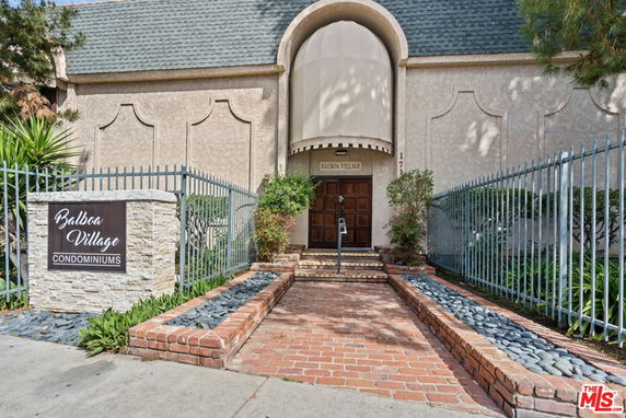 Front view of Balboa Village Condominiums entrance with a decorative fence and pathway.