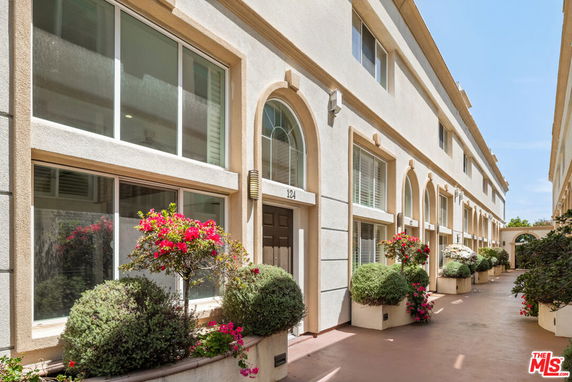 Front view of a multi-story building with arched windows and doors, accompanied by neatly arranged potted plants.
