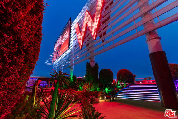 Neon-lit rooftop area with a large sign and decorative plants.