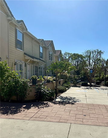 Front view of a two-story townhouse with plants and a paved walkway.