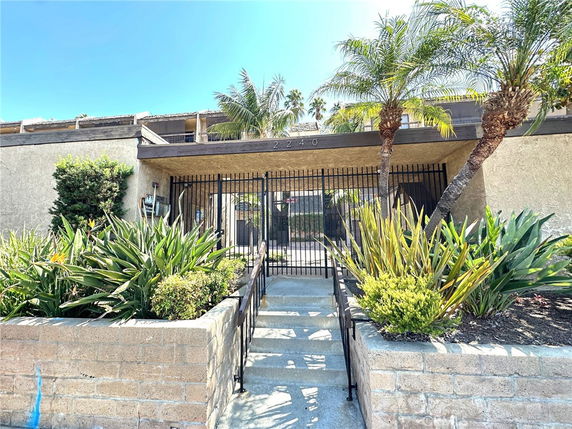 Front view of a building with gated entrance and stairs, surrounded by plants.